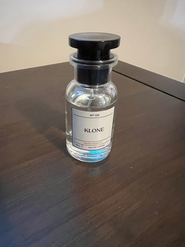 Customer's Klone Scents Collection perfume bottle with a black cap, standing on a dark wooden surface.