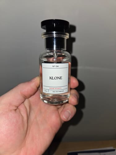 Customer's hand holding a clear, glass bottle of Klone Scents Collection Eau de Parfum with a label.