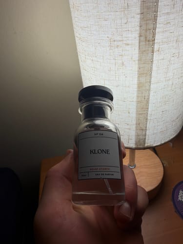 Customer's hand holding a bottle of Rouge Atlantic fragrance with a clear glass design and black cap.